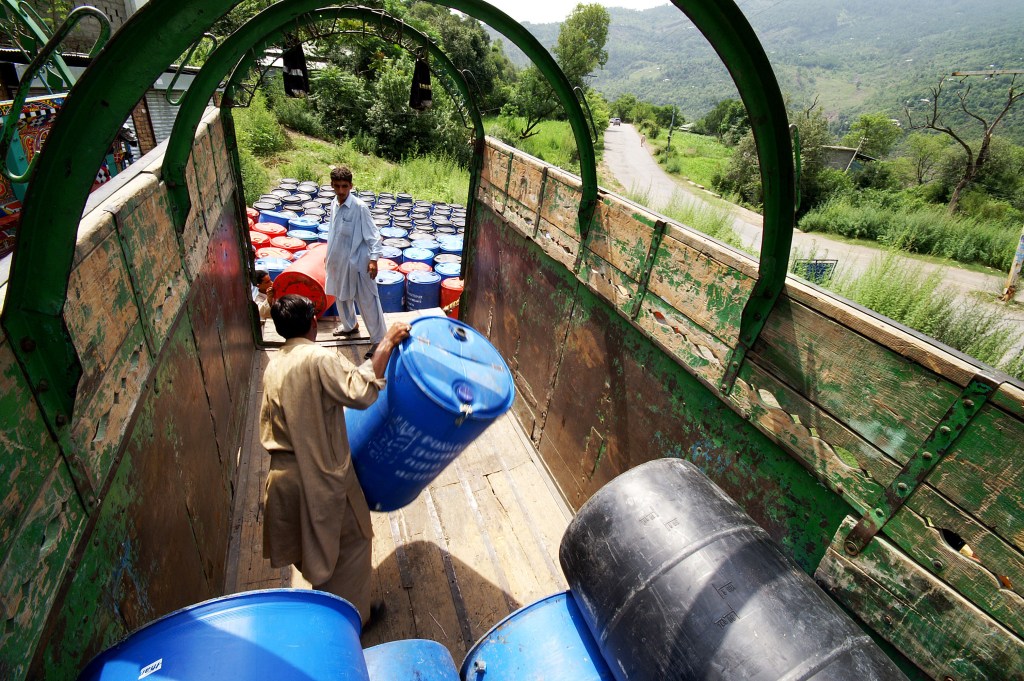 One man offloading blue containers from the back of a truck, while another waits with other containers.